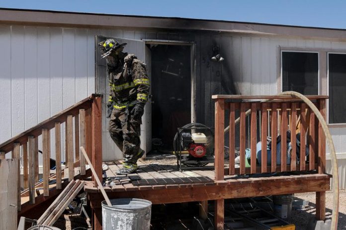 A firefighter exits the burned mobile home in Verde Villages 1 covered in insulation and soot Monday, July 5.