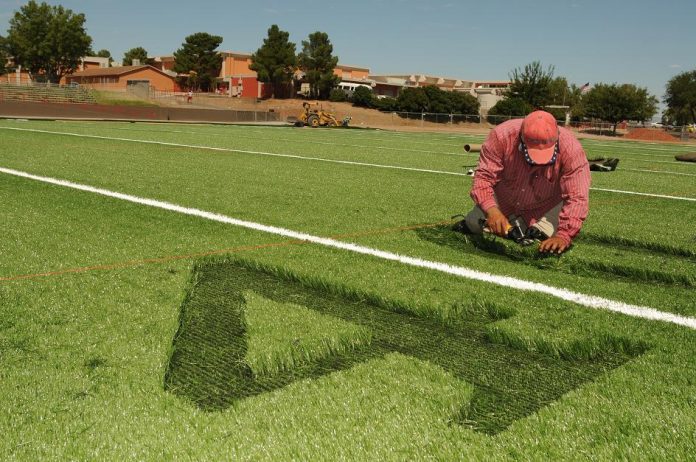 Laborer Rogelio Morales shaves the field marker numbers out of the artificial turf of the new football field currently being installed at Mingus Union High School on Friday, Sept. 3. The new field cost the school district $1.2 million.