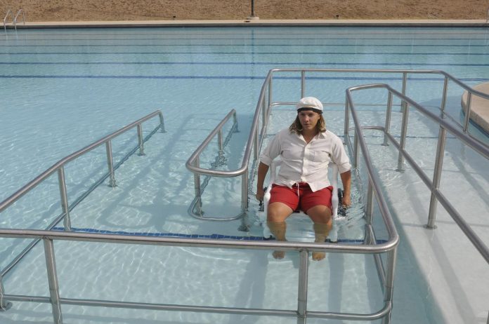 Lifeguard and manager Cole Rickey demonstrates how the handicapped-accessible ramp works on Saturday, Aug. 17. Rickey uses a hollow wheelchair that fills with water as the swimmer descends, making it fully submersible and preventing haphazard floating.