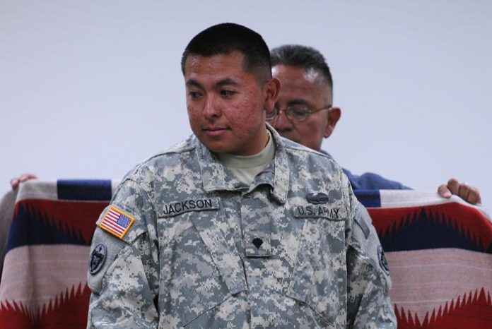 Lawrence Jackson Sr. wraps his son, returning Iraq War veteran U.S. Army Spc. Lawrence Jackson Jr., in a blanket to prepare him for a blessing from tribal elder Vincent Randall on Saturday, June 19.