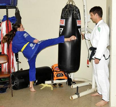 Ted Osburn, right, holds a punching bag as yellow belt Trinity Melgoza kicks it with all her might at Osburn’s Brazilian jiu-jitsu academy in Cottonwood.