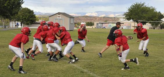 Head coach Mark Simmons hands the football off to eighth-grader Chaz Taylor, right, of Cottonwood Middle School to demonstrate a running play during the Lobos' practice of their shotgun spread offense. The team is undefeated through its first five games.