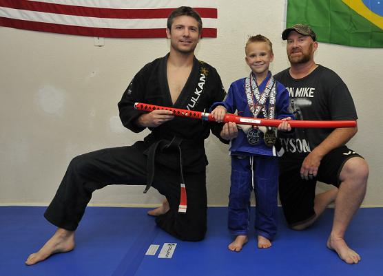 Stone Durkalec, 6, holds the samural sword he won at a recent grappling tournament in Phoenix with Brazilian jiu-jitsu instructor Ted Osburn, left, and father Stan Durkalec.