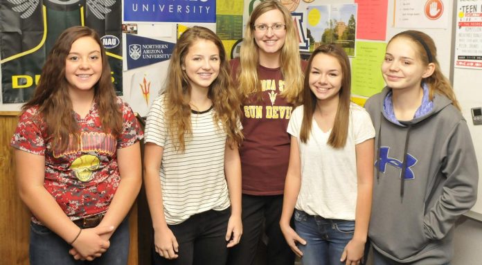 Cottonwood Middle School eighth-graders Jasmine Shults, Aspen Benevento, Rachael Sealy and Delaney Johnson, front from left, stand with their teacher Cristin Combs, center, in front of a wall decorated with posters and pennants of colleges from across the country. On May 4, Cottonwood-Oak Creek School District received the Arizona College Access Network and Arizona Gear Up “Early College and Career Awareness” award.